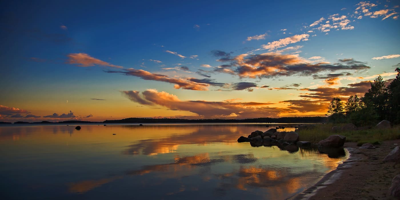Calm Finnish lake surface reflecting muted sky tones near pine shoreline.